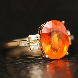 May include: An oval-shaped orange gemstone ring set in yellow gold with smaller diamond accents.