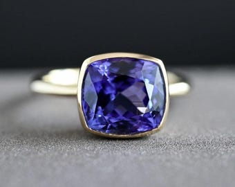 Puede incluir: Un anillo de oro con una gran piedra preciosa de color púrpura de forma cojín.
