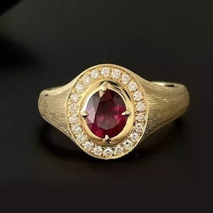 Puede incluir: Un anillo de oro con una piedra preciosa roja rodeada por un halo de pequeños diamantes.
