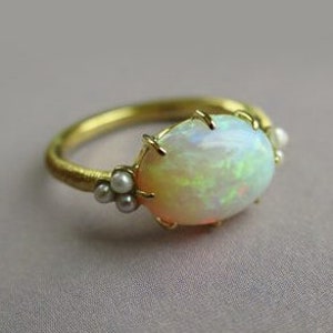 May include: A gold ring featuring an oval opal gemstone and small pearl accents.