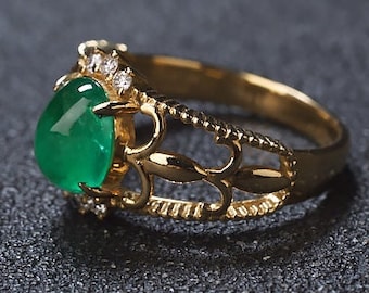 May include: A gold ring with a large, green emerald gemstone surrounded by smaller, clear diamonds. The ring has a delicate, intricate design.