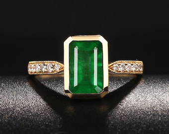 May include: A gold ring with a large emerald green gemstone set in a rectangular shape. The band is accented with small diamonds.