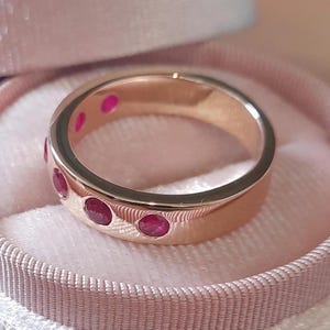 May include: A rose gold band ring with six red ruby stones set into the band.