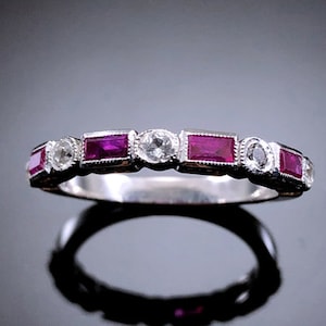 May include: A silver band ring with alternating ruby and diamond stones. The rubies are rectangular and the diamonds are round.