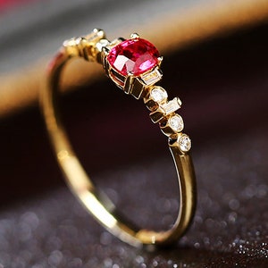 May include: A gold ring with a red ruby gemstone and small diamonds. The ring has a delicate design with a thin band and a cluster of diamonds on one side.