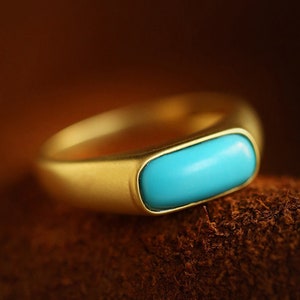 May include: A gold ring with a turquoise stone set in a rectangular shape.