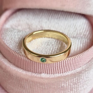 May include: A gold band ring with a small green gemstone set in the center.