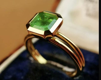 May include: A gold ring with a square emerald green gemstone set in a bezel setting.