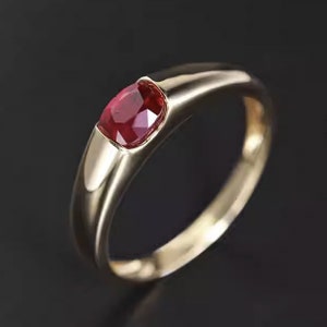 Op de afbeelding: Een gouden ring met een enkele, dieprode edelsteen in het midden gezet. De ring heeft een eenvoudig, klassiek ontwerp.