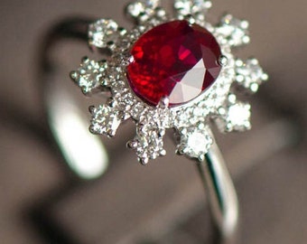 Puede incluir: Un anillo de plata con un gran rubí ovalado rodeado de diamantes más pequeños. El anillo tiene un diseño de copo de nieve.