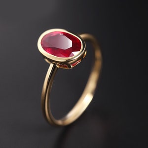 Pode incluir: Um anel de ouro com uma grande gema de rubi de forma oval, engastada em um engaste de bezel. O anel tem uma banda simples.