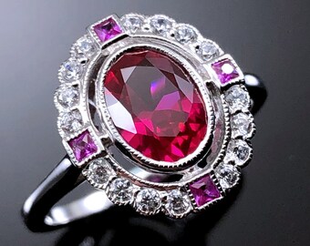 Puede incluir: Un anillo de plata con un gran rubí ovalado rodeado por un halo de diamantes más pequeños y zafiros rosas.