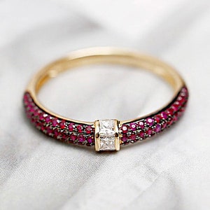 Peut inclure: Une bague en or avec un seul diamant de forme carrée serti au centre. La bande est incrustée de petits rubis rouges.