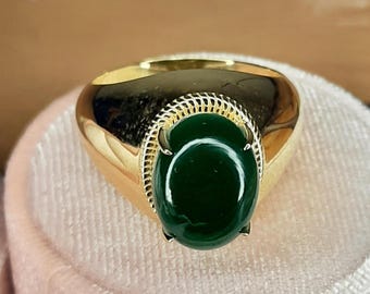 May include: A gold ring with a large, oval-shaped green gemstone set in a gold bezel. The ring has a textured band.
