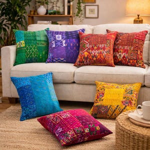 Peut inclure: Plusieurs coussins décoratifs colorés avec des motifs patchwork. Des coussins verts, bleus, violets, rouges et jaunes sont disposés sur un canapé crème et un tapis tissé. Les coussins présentent divers motifs géométriques et floraux.