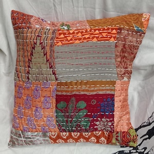 May include: A patchwork pillow cover with a variety of colorful fabrics, including orange, red, brown, and purple. The pillow cover is made of cotton and is quilted with a white thread.