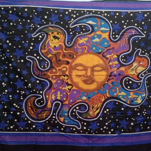 May include: A tapestry featuring a psychedelic sun with a closed-eye face surrounded by stars and clouds on a black background.
