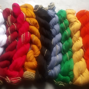 Puede incluir: Una colección de diez pañuelos coloridos con ribete de cuentas doradas. Los pañuelos están dispuestos en fila, con el pañuelo blanco a la izquierda y el pañuelo rosa a la derecha.