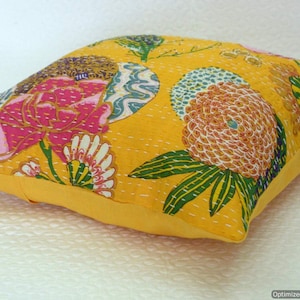 May include: A yellow cotton cushion cover with a floral pattern. The pattern features pink, orange, green, and white flowers on a yellow background.