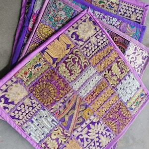 May include: A set of four purple patchwork cushion covers with intricate embroidery and gold accents. The covers are made of different fabrics and feature a variety of patterns.
