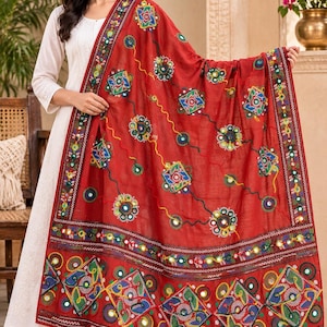 May include: A rectangular red shawl featuring intricate multi-coloured embroidery in geometric and floral patterns. The fabric is adorned with small circular mirrors throughout the design, complemented by a wide, decorative border with detailed stitching.