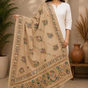 May include: A beige rectangular shawl featuring intricate multi-colored floral embroidery and small circular mirrors. The fabric displays a decorative border with geometric patterns, interspersed with reflective mirror accents throughout the design.