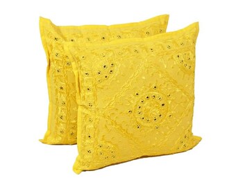 May include: Two square yellow decorative pillows. The pillows have a textured surface with a pattern of small, dark-colored embellishments. The pillows are made of a soft fabric and are placed against a white background.
