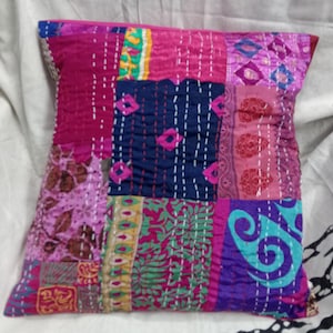May include: A patchwork pillow cover with a variety of colors and patterns, including pink, blue, green, and purple. The cover is made of fabric scraps sewn together in a random pattern.