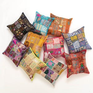 Könnte beinhalten: Eine Sammlung von zehn bunten Patchwork-Wurfkissen mit verschiedenen Stickereien. Die Kissen sind in einem Halbkreis auf weißem Hintergrund angeordnet.