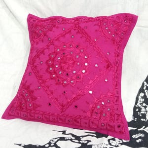 May include: A pink square throw pillow with a decorative embroidered design featuring small mirrored accents.