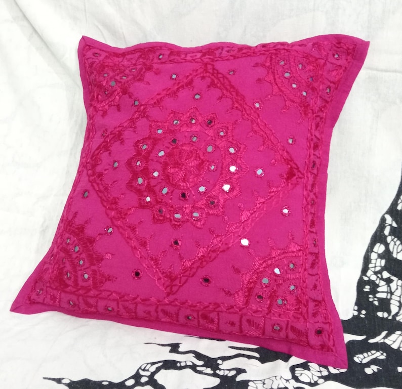 May include: A pink square throw pillow with a decorative embroidered design featuring small mirrored accents.