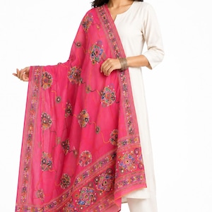 Puede incluir: Un dupatta de color rosa intenso vibrante con intrincados bordados florales multicolores y pequeños detalles de espejos circulares. La tela es ligera y semitransparente, con un patrón de borde decorativo a lo largo de los lados del chal rectangular.
