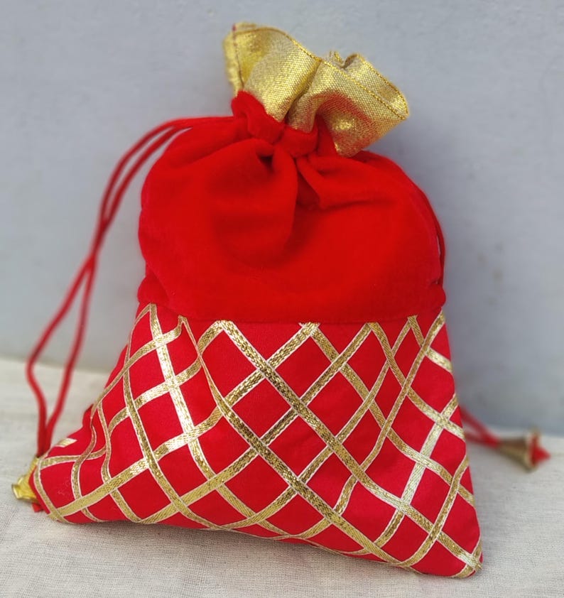 May include: Red velvet drawstring bag with a gold patterned bottom. The bag is closed with a drawstring and has a gold tassel.
