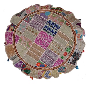 May include: Round patchwork floor cushion with a variety of colorful fabric squares. The cushion has a brown border and is adorned with small tassels in various colors. The design includes floral and geometric patterns.