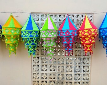 May include: Seven colorful fabric lanterns with intricate designs and mirror accents hanging from a string. The lanterns are in shades of blue, green, pink, yellow, and red.