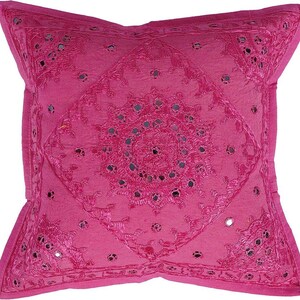 May include: A pink throw pillow with a circular design of embroidered flowers and mirrored accents.