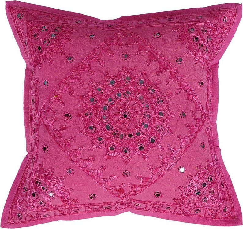 May include: A pink throw pillow with a circular design of embroidered flowers and mirrored accents.