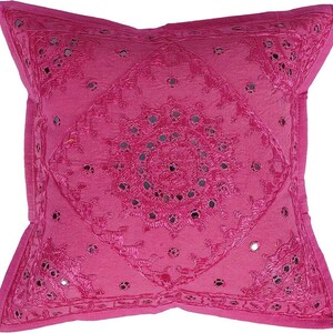May include: A pink throw pillow with a circular design of embroidered flowers and mirrored accents.