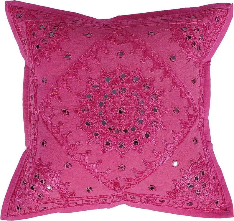May include: A pink throw pillow with a circular design of embroidered flowers and mirrored accents.