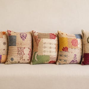 Op de afbeelding: Vijf decoratieve sierkussens met patchwork-ontwerpen. De kussens hebben een verscheidenheid aan kleuren, waaronder beige, roze, paars, groen en geel. Elk kussen heeft een uniek patroon en textuur, wat zorgt voor een gezellige en eclectische uitstraling.