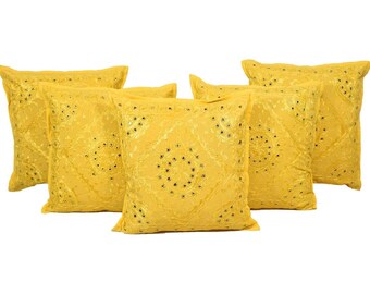 May include: Six yellow decorative throw pillows. Each pillow has a square shape with a textured pattern and small, dark embellishments arranged in a circular design. The pillows are arranged on a white background.