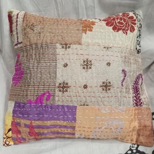 May include: A patchwork pillow cover with a variety of colors and patterns, including brown, beige, purple, pink, and orange. The cover is made of cotton and has a quilted design.