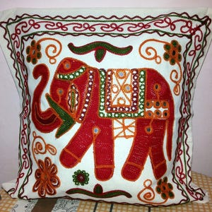May include: White cotton pillow cover with an embroidered red elephant design. The elephant is decorated with colorful beads and small mirrors. The pillow cover has a decorative border with green and red embroidery.