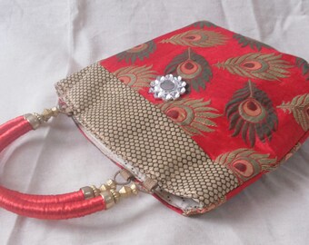 Puede incluir: Bolso de mano rojo con estampado de plumas de pavo real. El bolso presenta un adorno de pedrería y asas rojas. El borde superior está adornado con una tela estampada. Un accesorio elegante.
