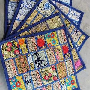 May include: A set of five colourful embroidered fabric coasters with a patchwork design. The coasters are square and have a blue border. The fabric is a mix of different colours and patterns, including gold, red, and green.