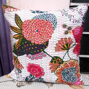 May include: Square decorative pillow with a white background and a vibrant floral pattern. The design features large, stylized flowers in shades of red, orange, pink, and green, with intricate stitching details. The pillow is likely made of a soft fabric.