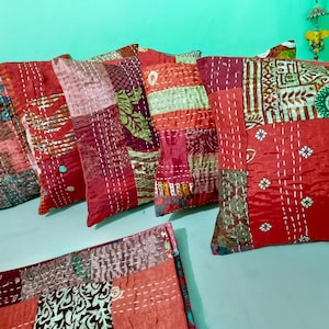 May include: A collection of square throw pillows and a rectangular cushion featuring a patchwork design of various red, pink, and brown fabric squares. Each piece is detailed with white running stitch embroidery throughout the surface.