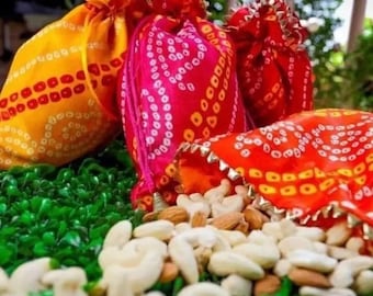 May include: Three colorful fabric pouches with a traditional Indian design, filled with cashews and almonds. The pouches are decorated with gold trim and are sitting on a bed of green grass.