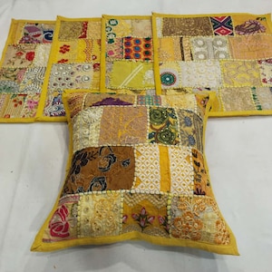 May include: A set of four yellow throw pillows with a patchwork design. Each pillow is made of different fabrics and colors, including gold, brown, and white. The pillows are decorated with embroidery and sequins.