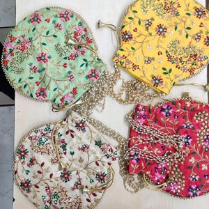 Può includere: Quattro sacchetti rotondi con coulisse e catene di perle ricamate. I sacchetti sono di colore verde, giallo, bianco e rosso con motivi floreali.